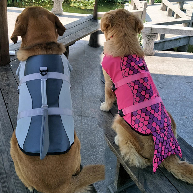 Two dogs wearing life vests, one gray shark and one pink with mermaid pattern, sitting on a wooden bench.